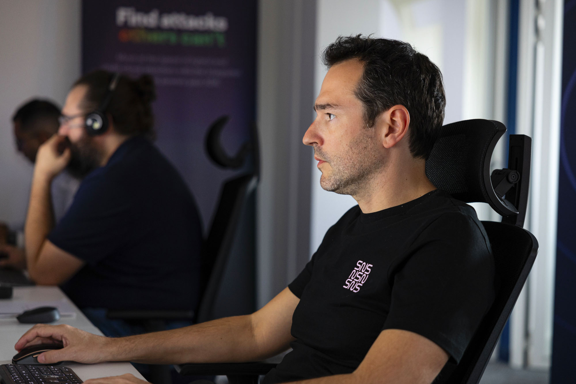 analyste SOC portant un t-shirt noir SNS Security à son poste de travail