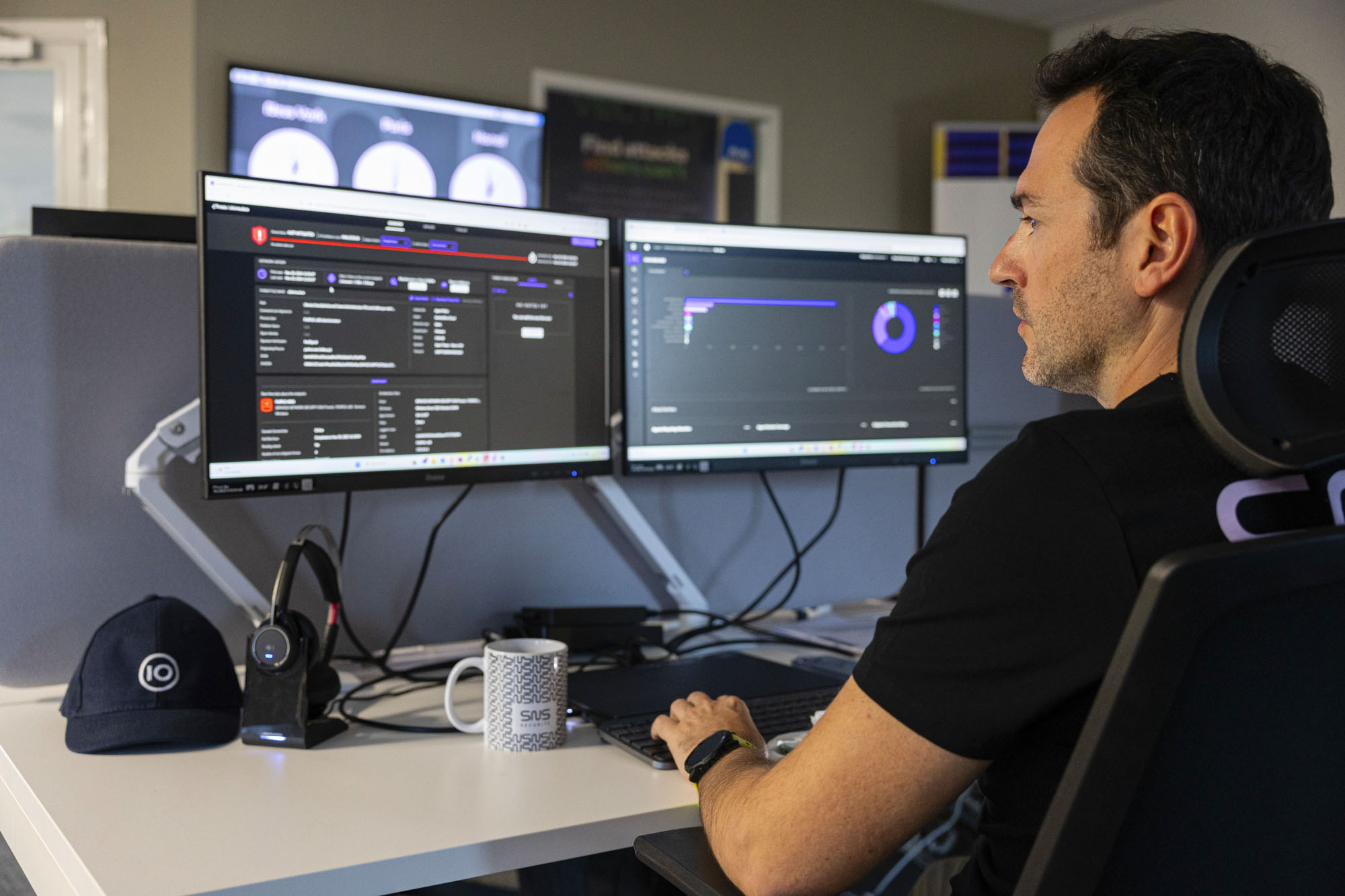 analyste SOC avec un t-shirt noir de dos regardant ses deux écrans d'ordinateur