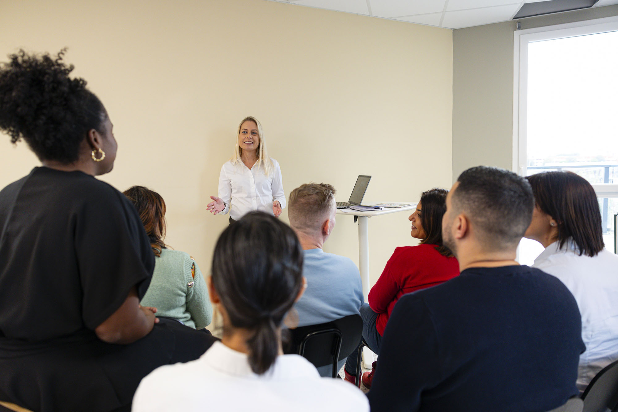 Public assis vu de dos lors d'une formation animée par une femme blonde en arrière-plan