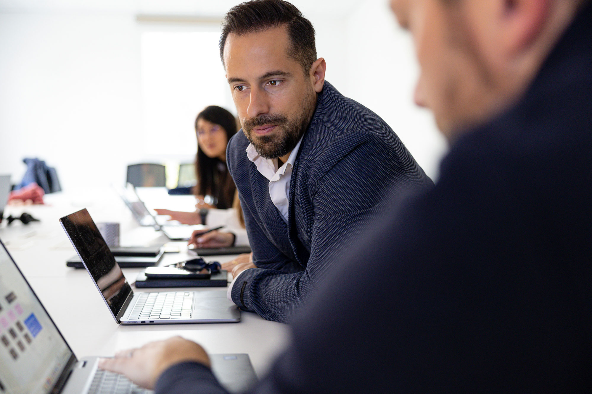 ingénieur commercial en costume assis à une table de réunion regardant l'écran de son collègue