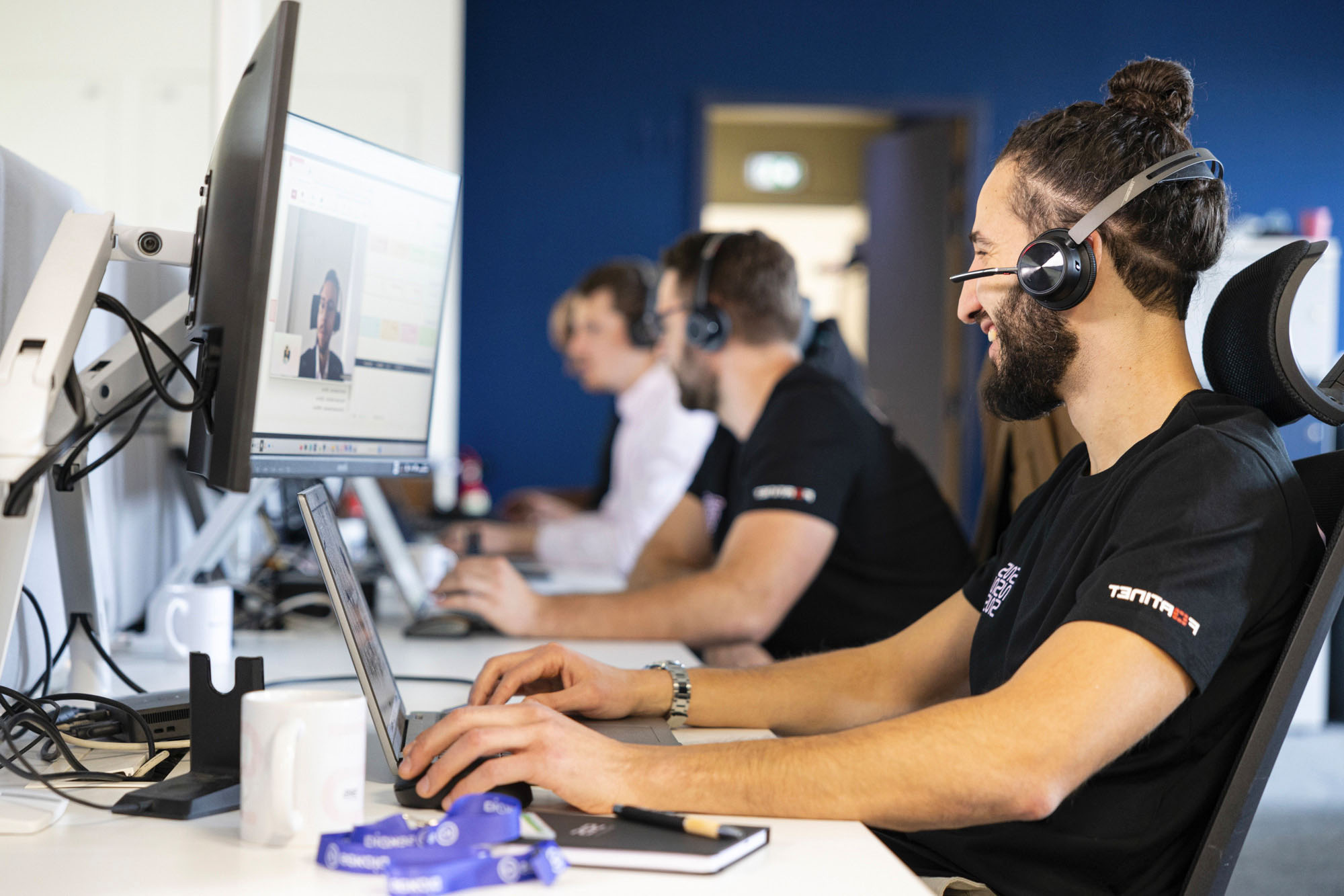 ingénieur support avec un casque qui sourit assis à son poste de travail à côté d'autres ingénieurs