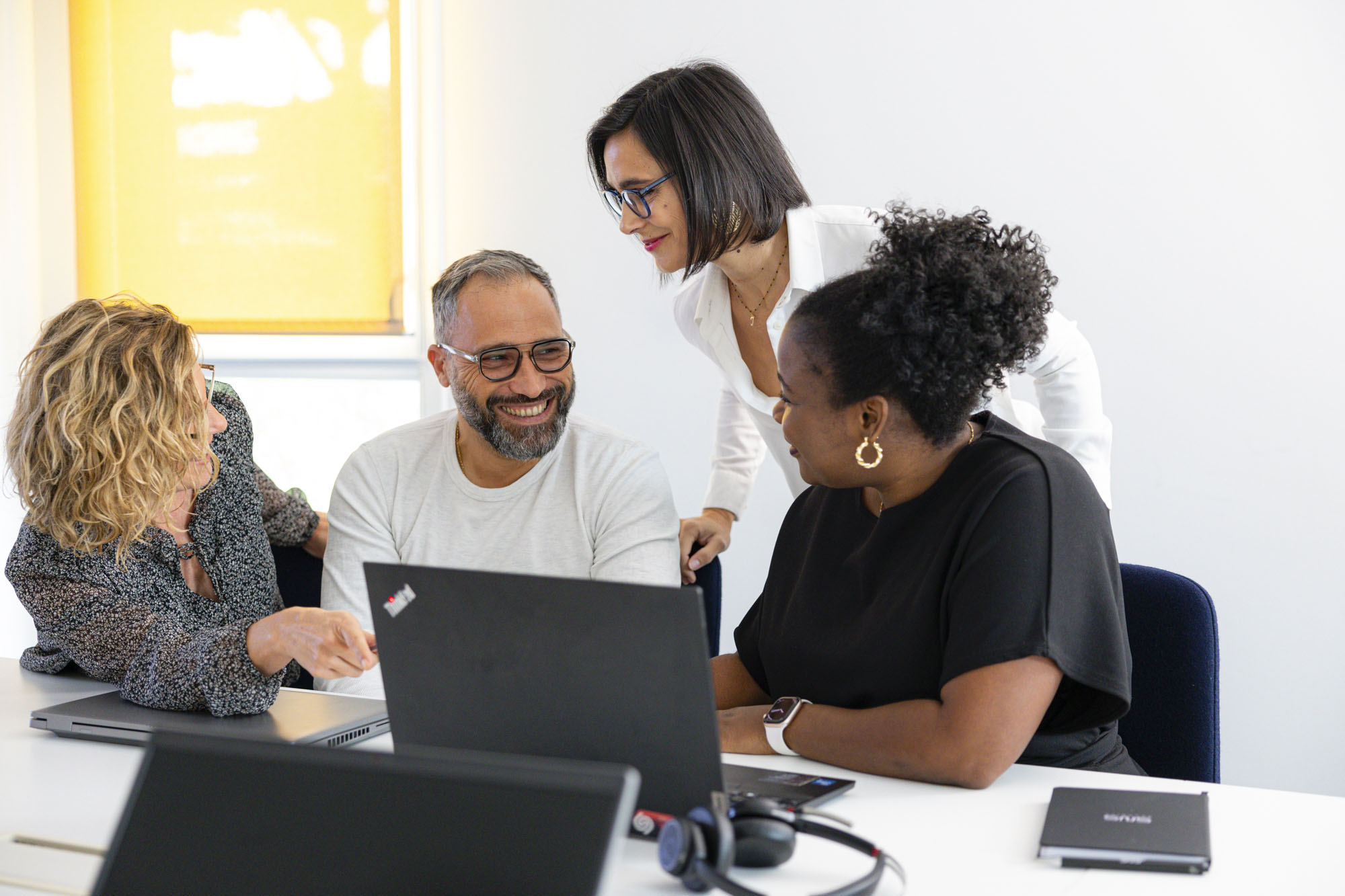 quatre collaborateurs SNS Security souriants discutant autour d'une table de réunion