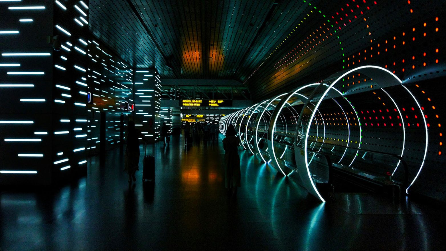 un hall dans le noir éclairé par des nombreux néons colorés sortant d'un tunnel