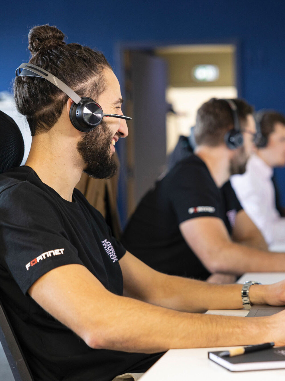 ingénieur support avec un casque qui sourit assis à son poste de travail à côté d'autres ingénieurs